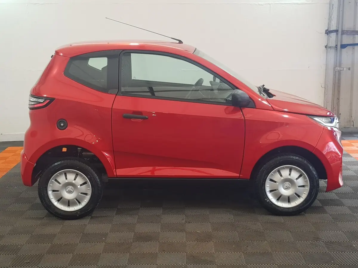 Vue de profil côté gauche d'une Aixam Ambition 0.5 City Pack rouge avec rétroviseur caméra côté conducteur.