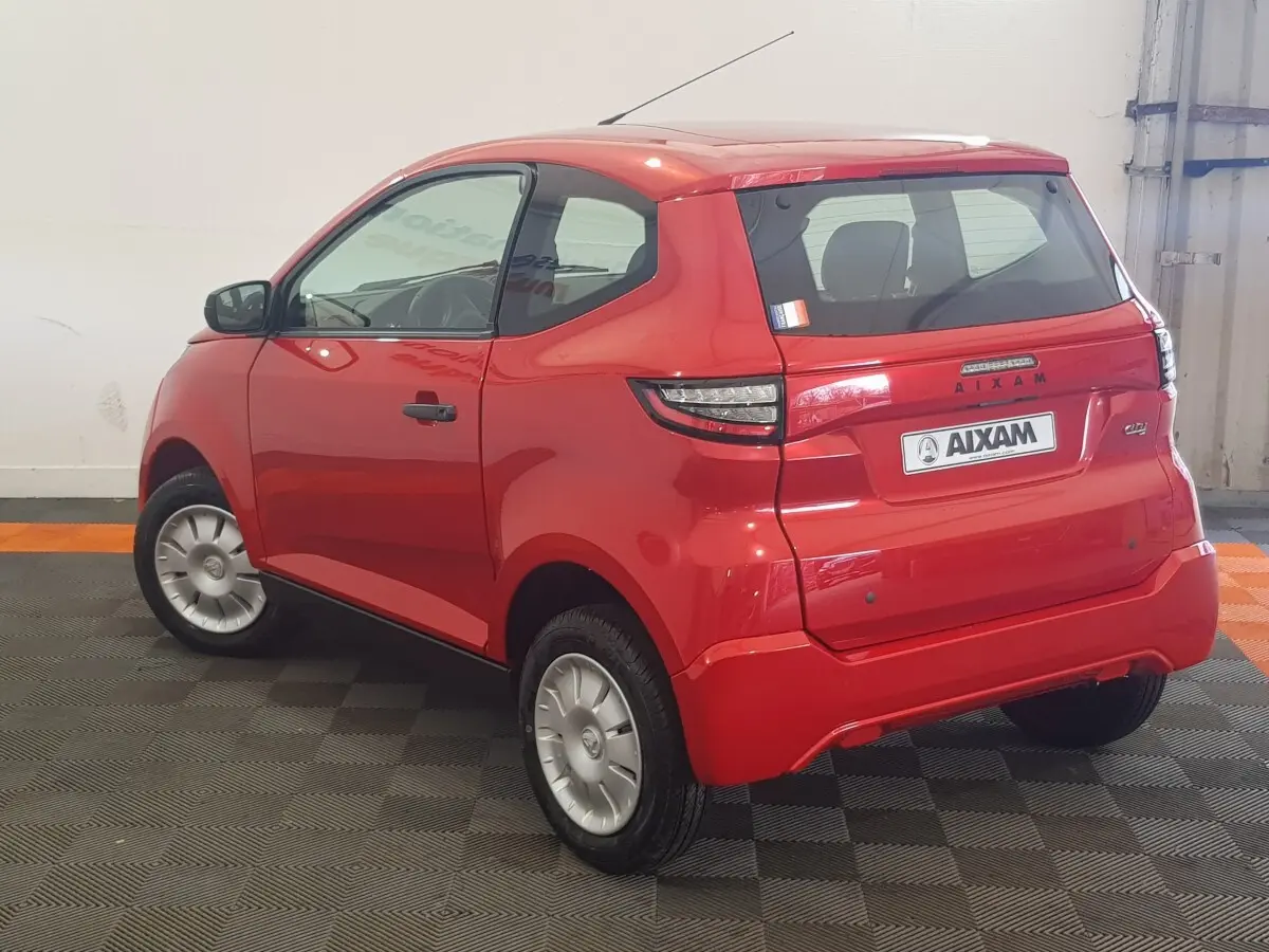 Vue 3/4 arrière droite d'une Aixam Ambition 0.5 City Pack rouge 2026 avec caméra sur rétroviseur côté gauche.