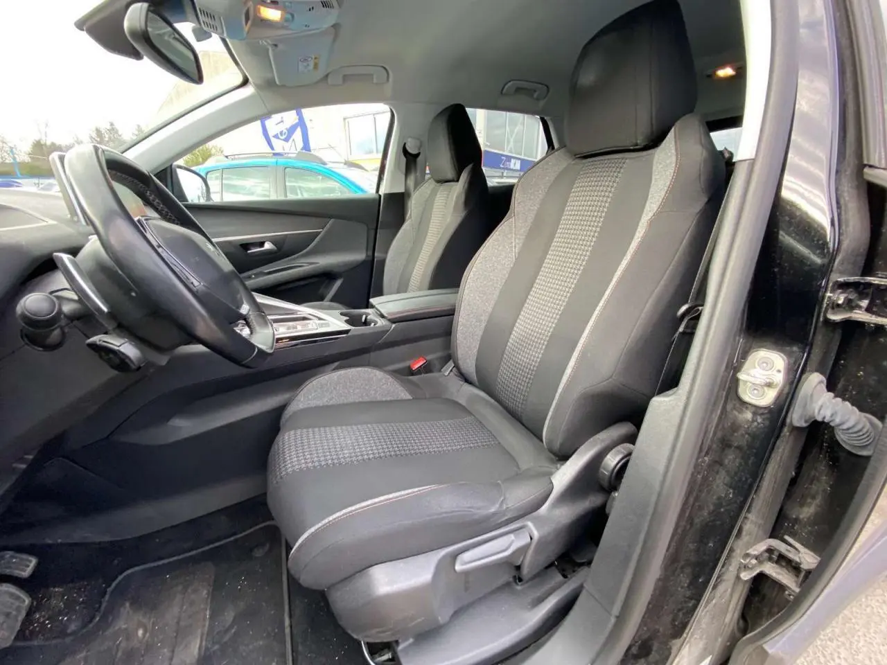 Intérieur du Peugeot 3008 noir 2019 vu côté conducteur, sièges tissu noir avec motifs et surpiqûres rouges visibles.