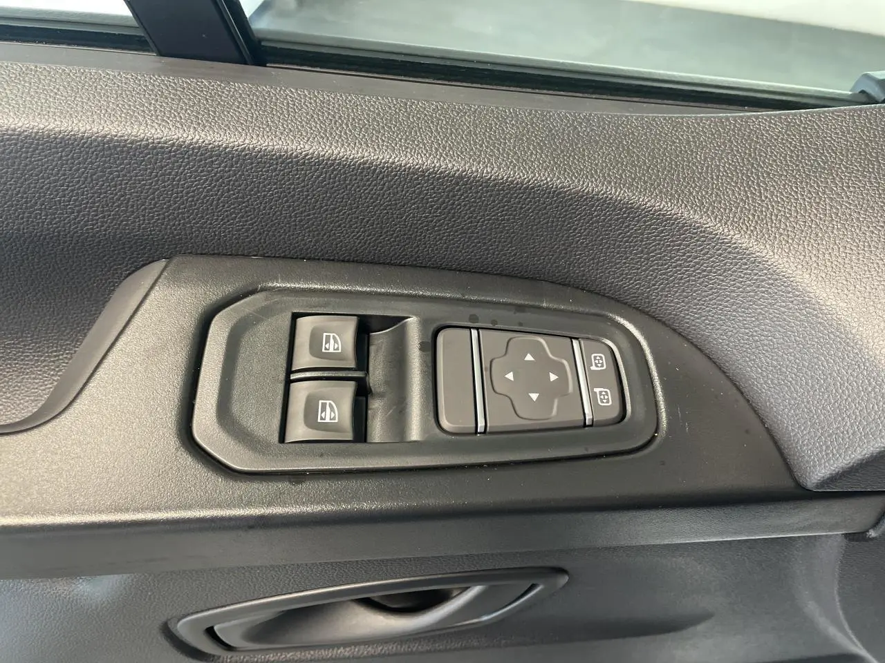 Gros plan sur les commandes de lève-vitres et réglage des rétroviseurs côté conducteur du Renault Trafic blanc.