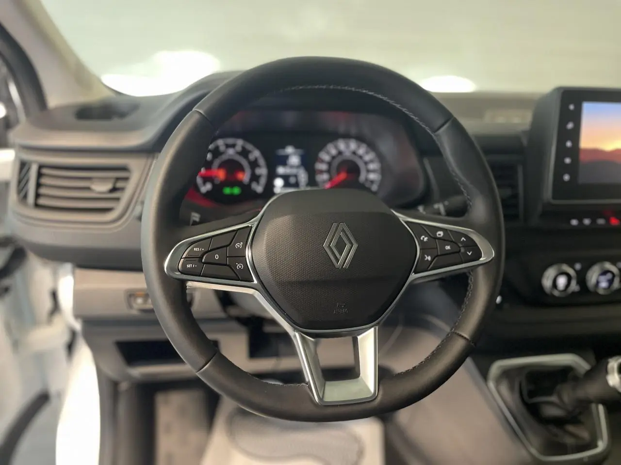 Vue centrée sur le volant noir du Renault Trafic Fourgon blanc, avec tableau de bord et écran tactile en arrière-plan.