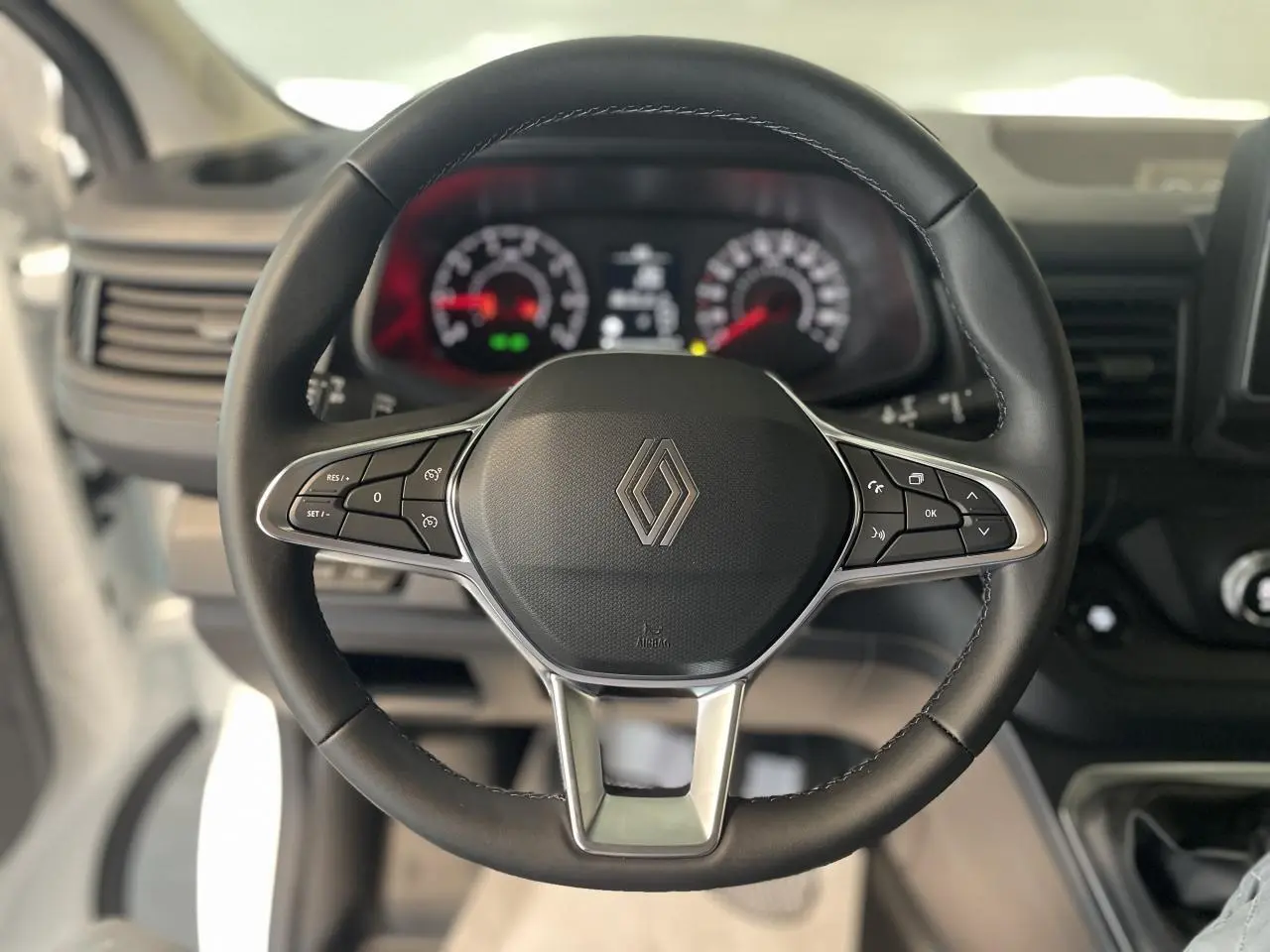 Volant noir avec logo Renault au centre, cadrans de tableau de bord flous en arrière-plan, intérieur du Renault Trafic Fourgon.