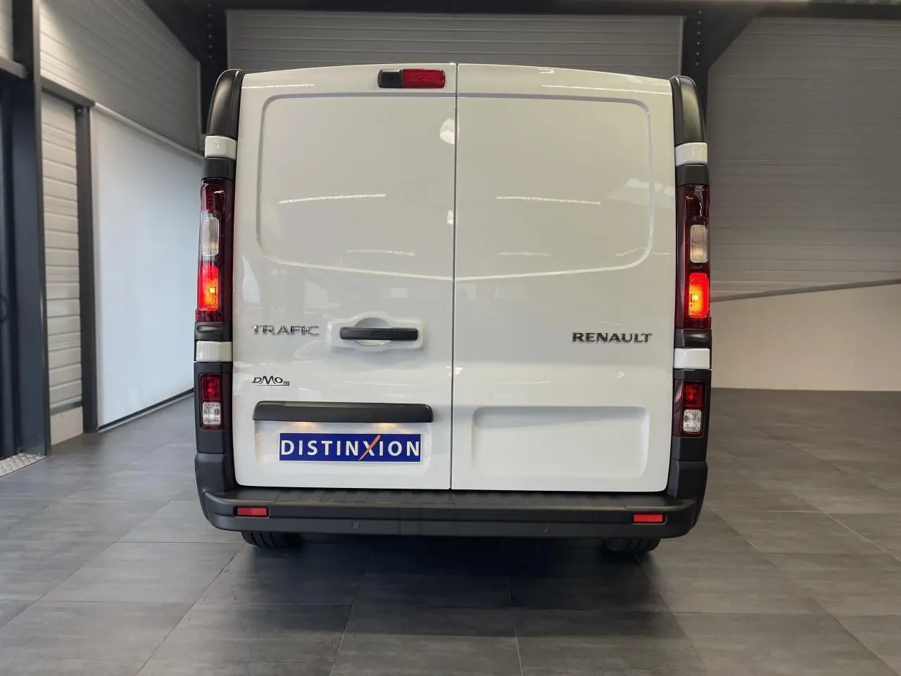 Vue arrière du Renault Trafic Fourgon blanc avec feux allumés et plaque Distinxion dans un garage.