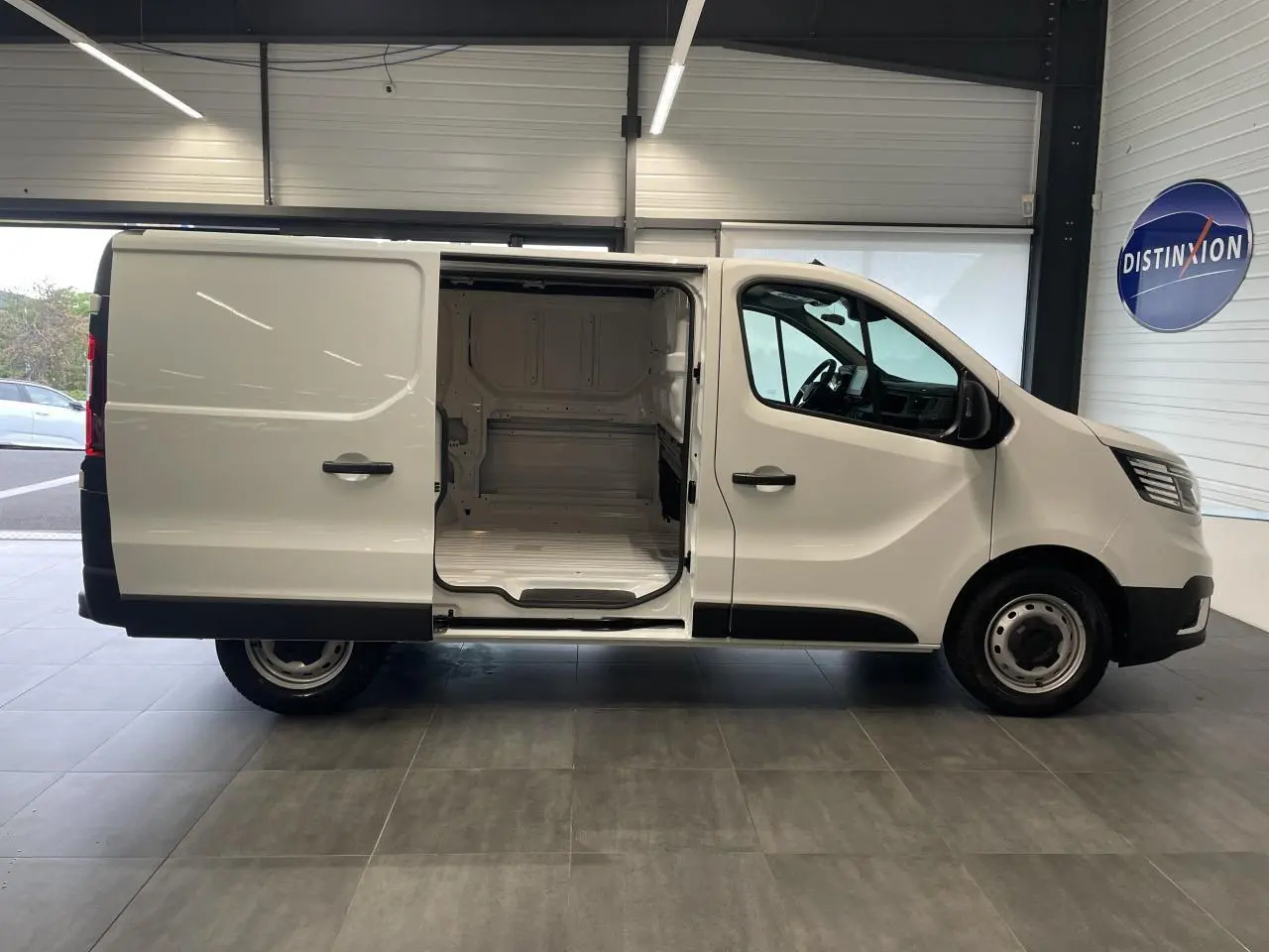 Renault Trafic Fourgon blanc en vue profil droit avec porte latérale coulissante ouverte montrant l'espace de chargement vide.