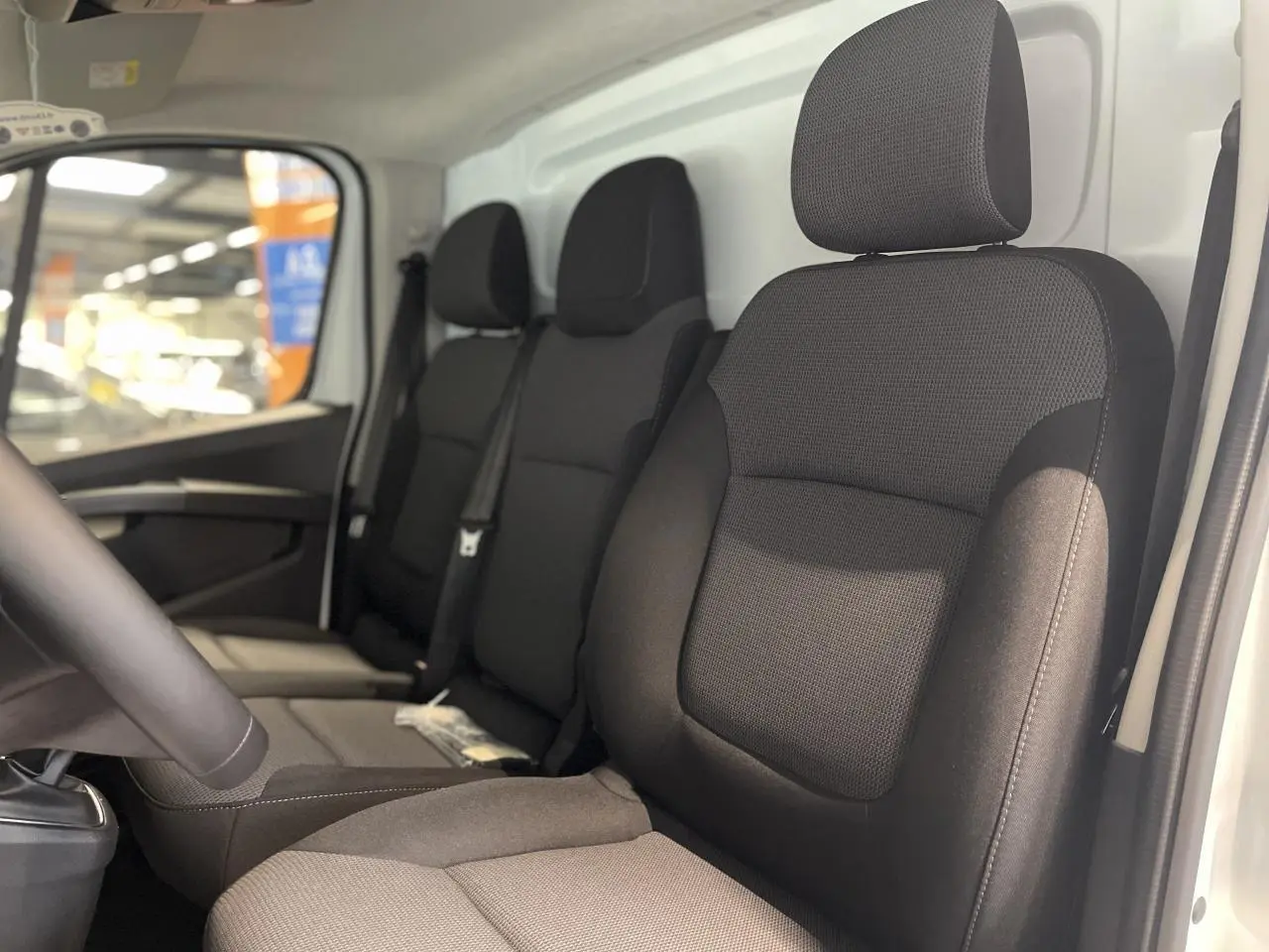 Vue intérieure côté conducteur du Renault Trafic Fourgon blanc, montrant les sièges noirs en tissu et la banquette passager.