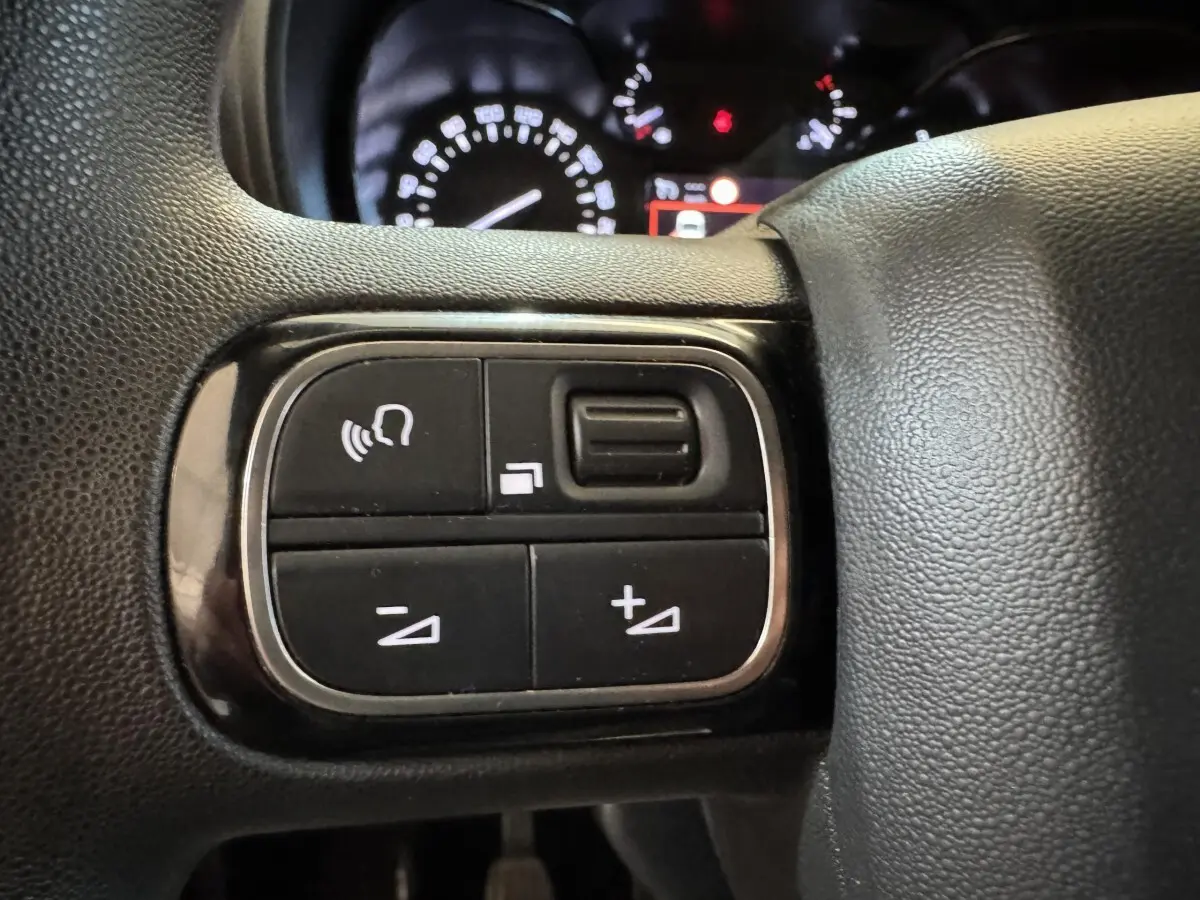 Gros plan sur les commandes multifonctions noires du volant du Citroën Berlingo 2020, avec tableau de bord en arrière-plan.