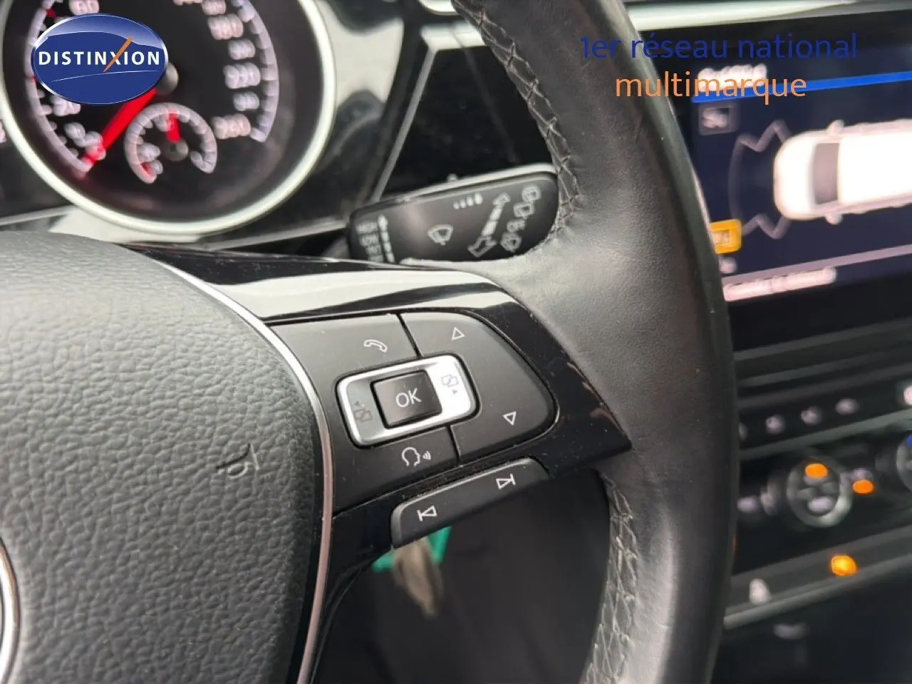 Gros plan sur le volant en cuir noir du Volkswagen Touran 2018 avec commandes intégrées et tableau de bord numérique en arrière-plan.