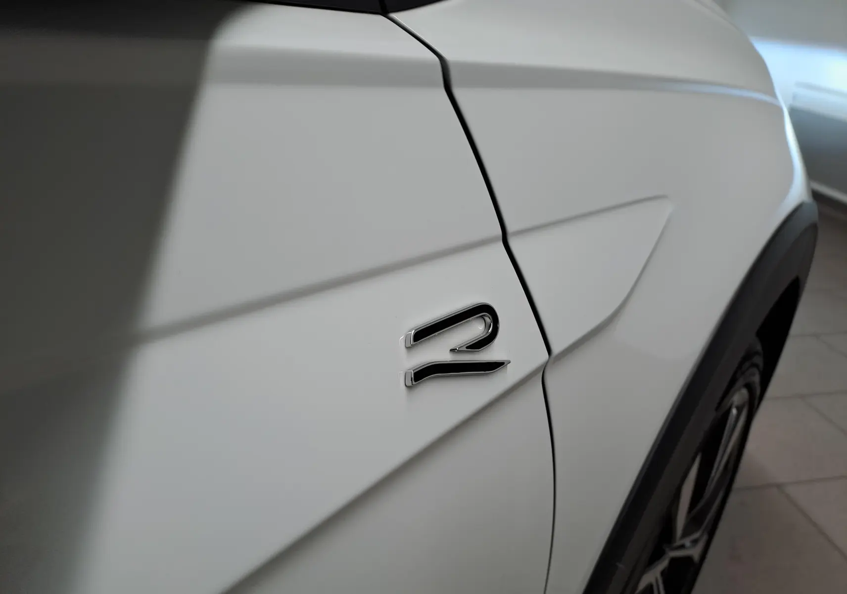 Gros plan sur l'aile avant droite blanche du Volkswagen Taigo 2025 avec logo R-Line et jante alliage visible.