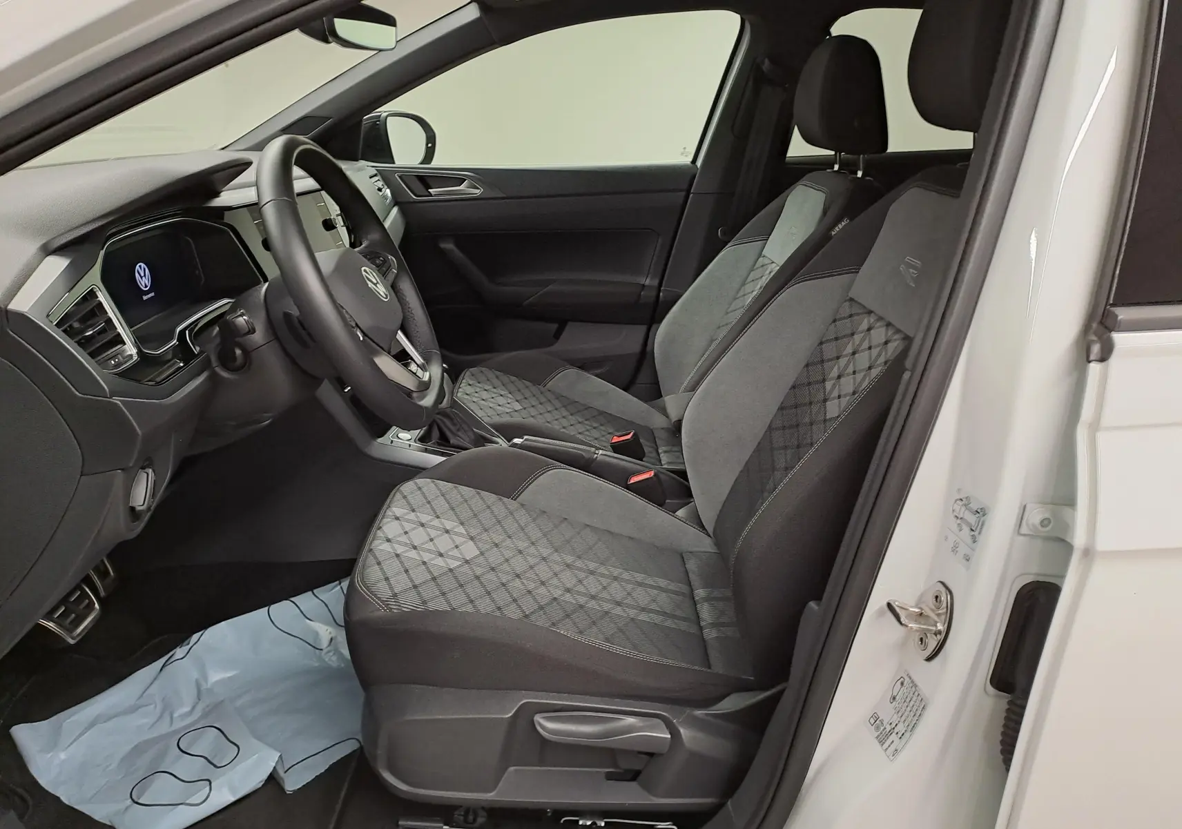 Vue intérieure côté conducteur du Volkswagen Taigo 1.5 TSI 150 DSG7 R-Line Edition avec sièges tissu gris à motifs et volant multifonction.