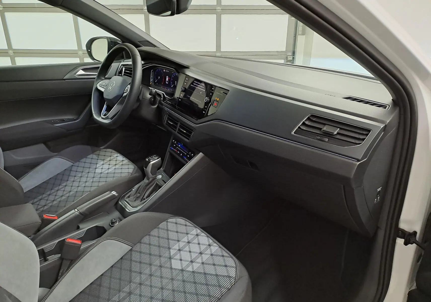 Vue intérieure côté conducteur du Volkswagen Taigo 2025, tableau de bord noir avec sièges tissu à motif gris.