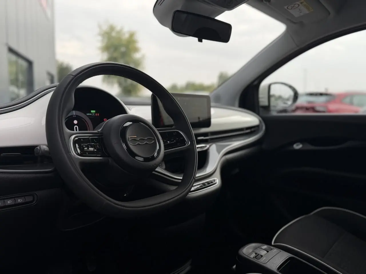 Intérieur de la Fiat 500 électrique 2024 vue côté conducteur, tableau de bord blanc et volant noir avec logo 500.