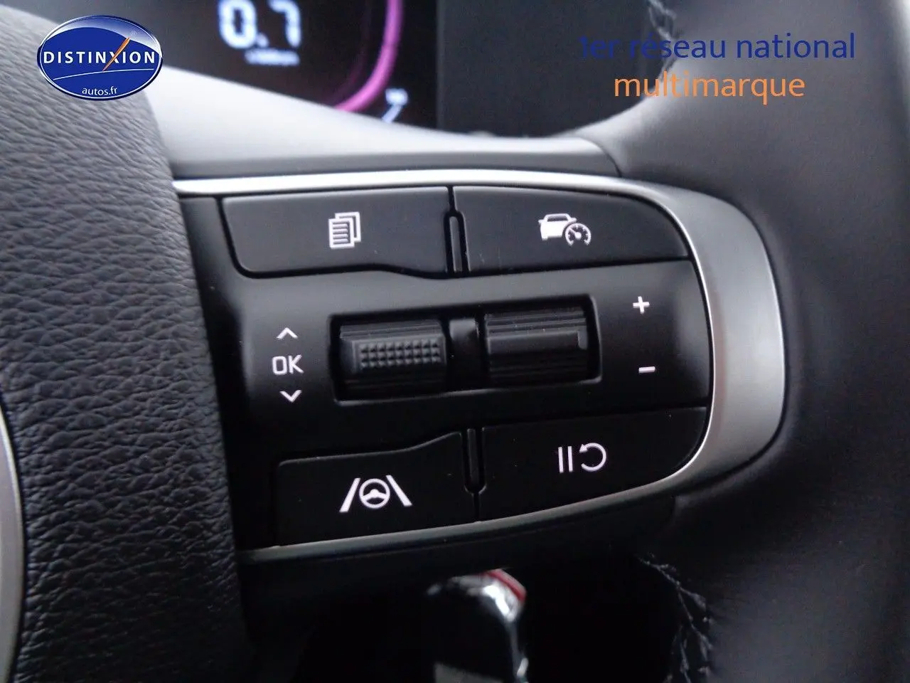 Gros plan sur les commandes au volant du Kia Sportage gris acier, mettant en valeur les boutons de régulateur et d’aide à la conduite.