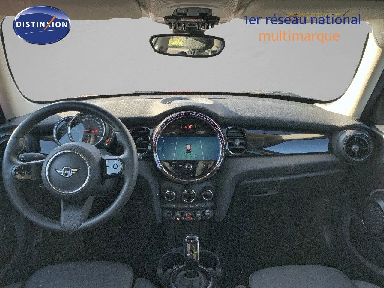 Vue intérieure frontale du tableau de bord de la MINI 1.5 136CH STEPTRONIC 2023 avec volant, écran central rond et finition noire.
