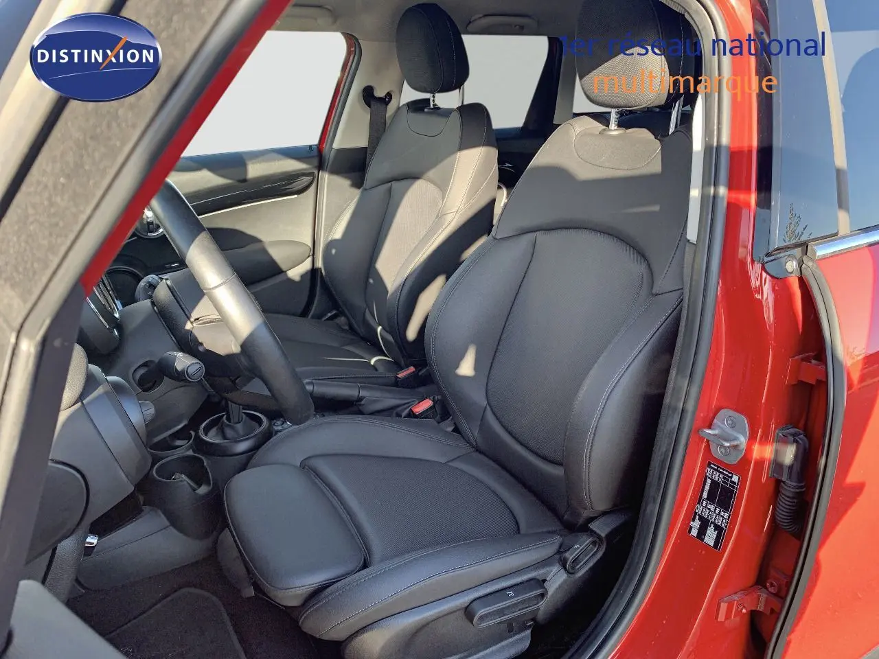 Vue intérieure côté conducteur d'une MINI rouge chili 2023 avec sièges avant en cuir noir et volant visible.