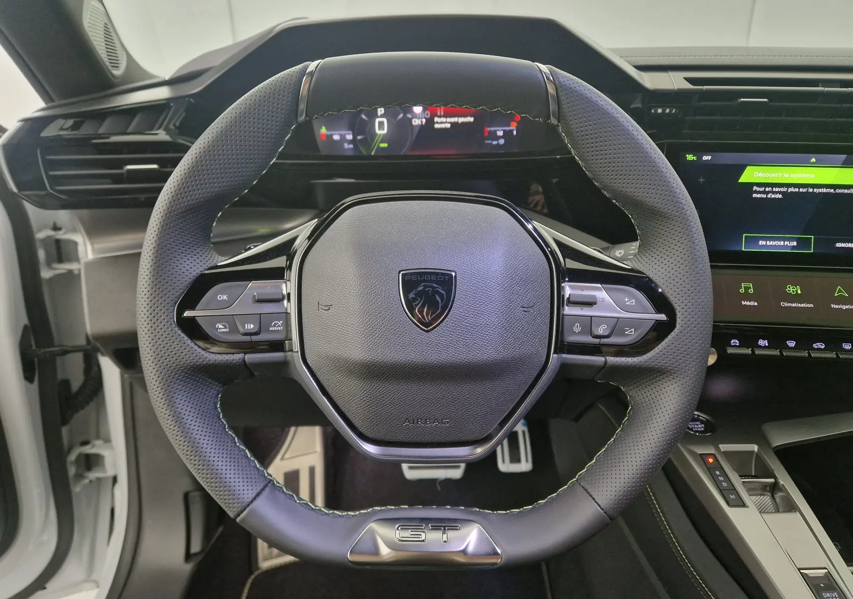 Vue rapprochée du volant cuir perforé noir avec logo Peugeot et badge GT de la 308 blanche 2025.