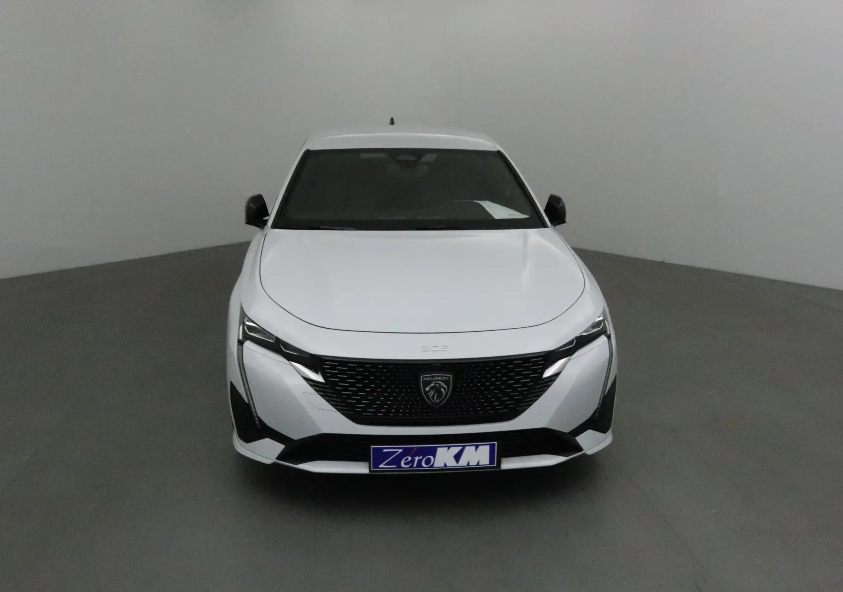 Vue frontale d'une Peugeot 308 blanche Okenite 2025 avec calandre noire et logo lion central bien visible.