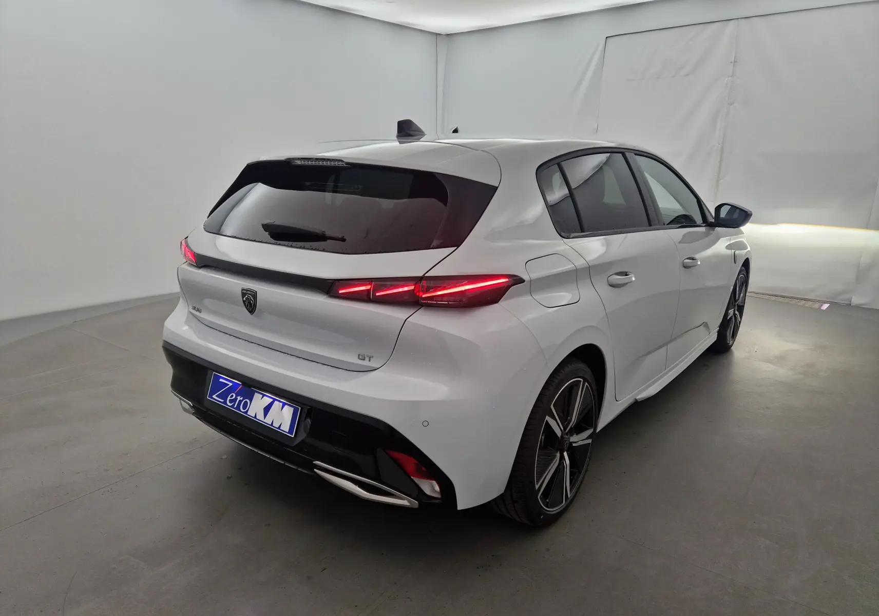 Vue 3/4 arrière droite d'une Peugeot 308 GT blanche Okenite avec feux LED allumés et jantes alliage noires.