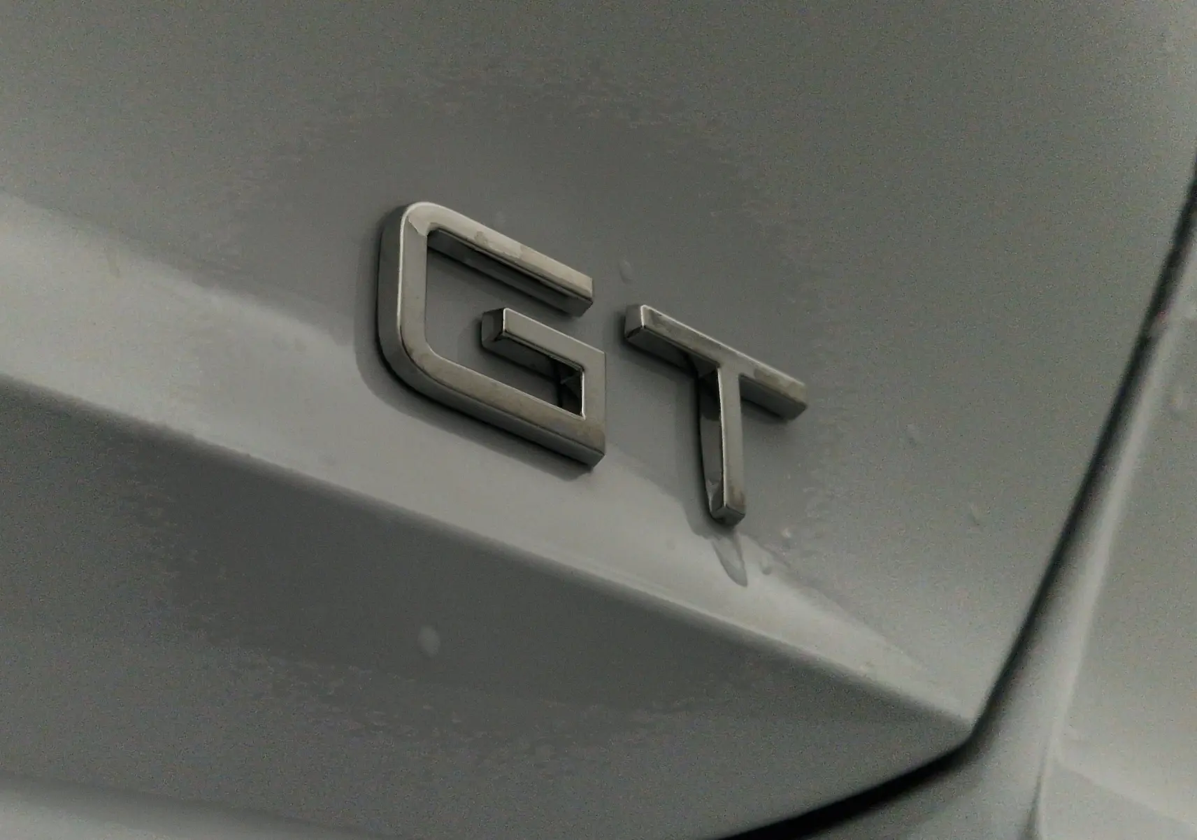 Gros plan sur l'emblème GT en métal sur la carrosserie blanche Okenite d'une Peugeot 308 2025.