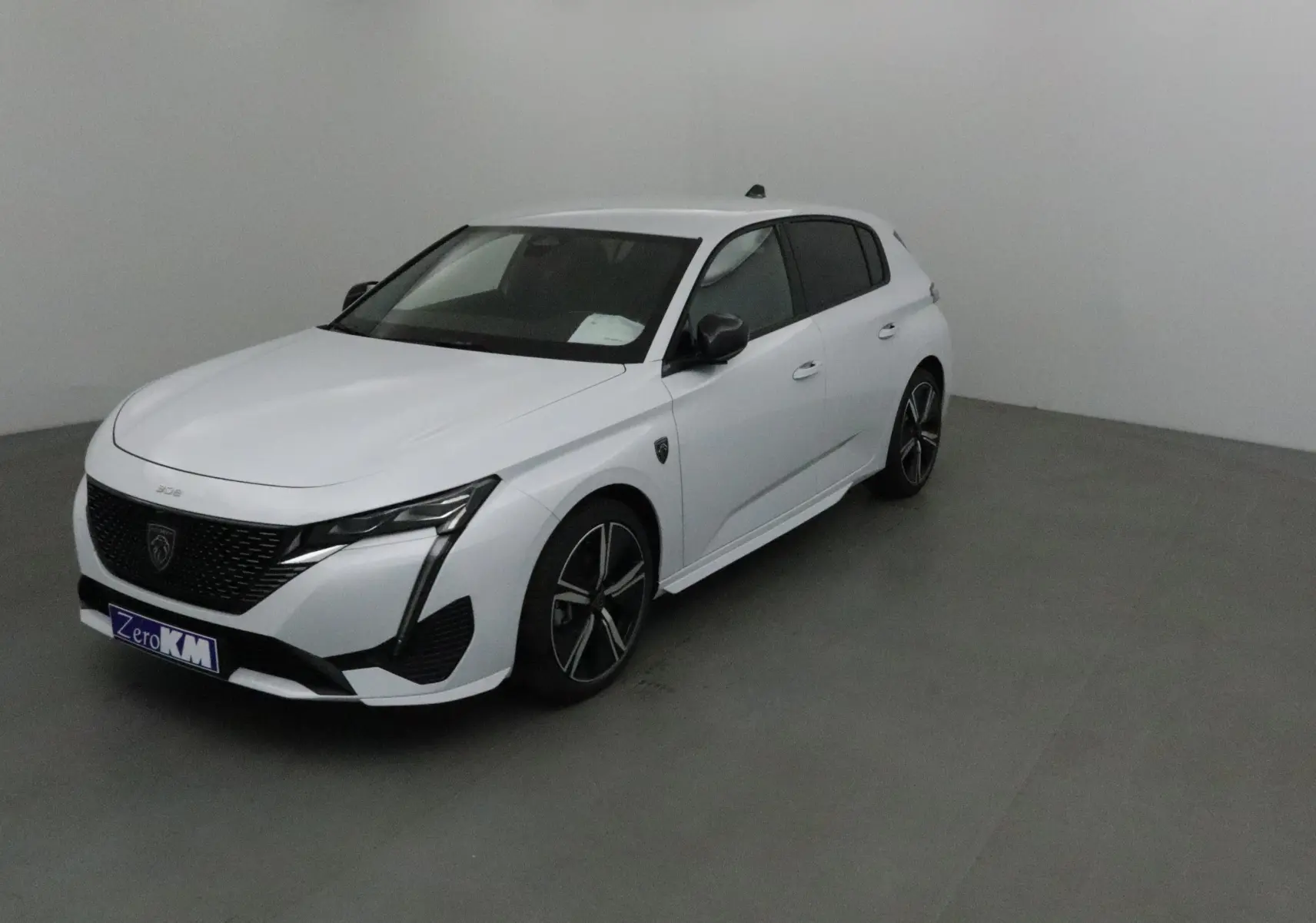 Peugeot 308 blanc Okenite vue 3/4 avant droit, avec jantes noires et détails noirs contrastants sur calandre et rétroviseurs.