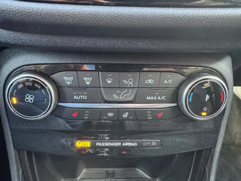 Panneau de commandes de climatisation et chauffage avec voyants allumés dans un Ford Puma rouge, vue intérieure rapprochée.