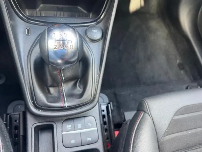 Le levier de vitesses manuel noir avec surpiqûres rouges dans l'habitacle du Ford Puma rouge 2023, côté conducteur.