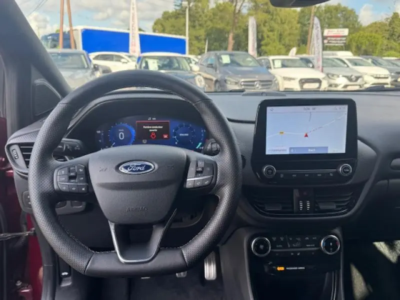 Vue intérieure frontale du tableau de bord et volant noir de la Ford Puma rouge avec écran tactile GPS allumé