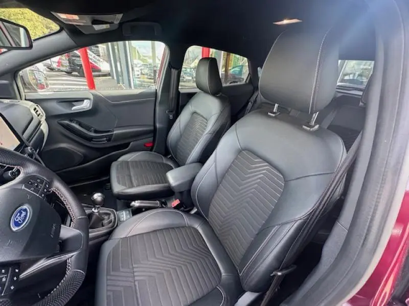 Intérieur avant du Ford Puma rouge 2023, sièges noirs en cuir avec surpiqûres et volant multifonction visible côté gauche.