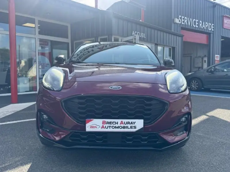 Vue frontale d'un Ford Puma rouge vif Ruby Edition avec calandre noire et logo Ford visible, devant un garage.
