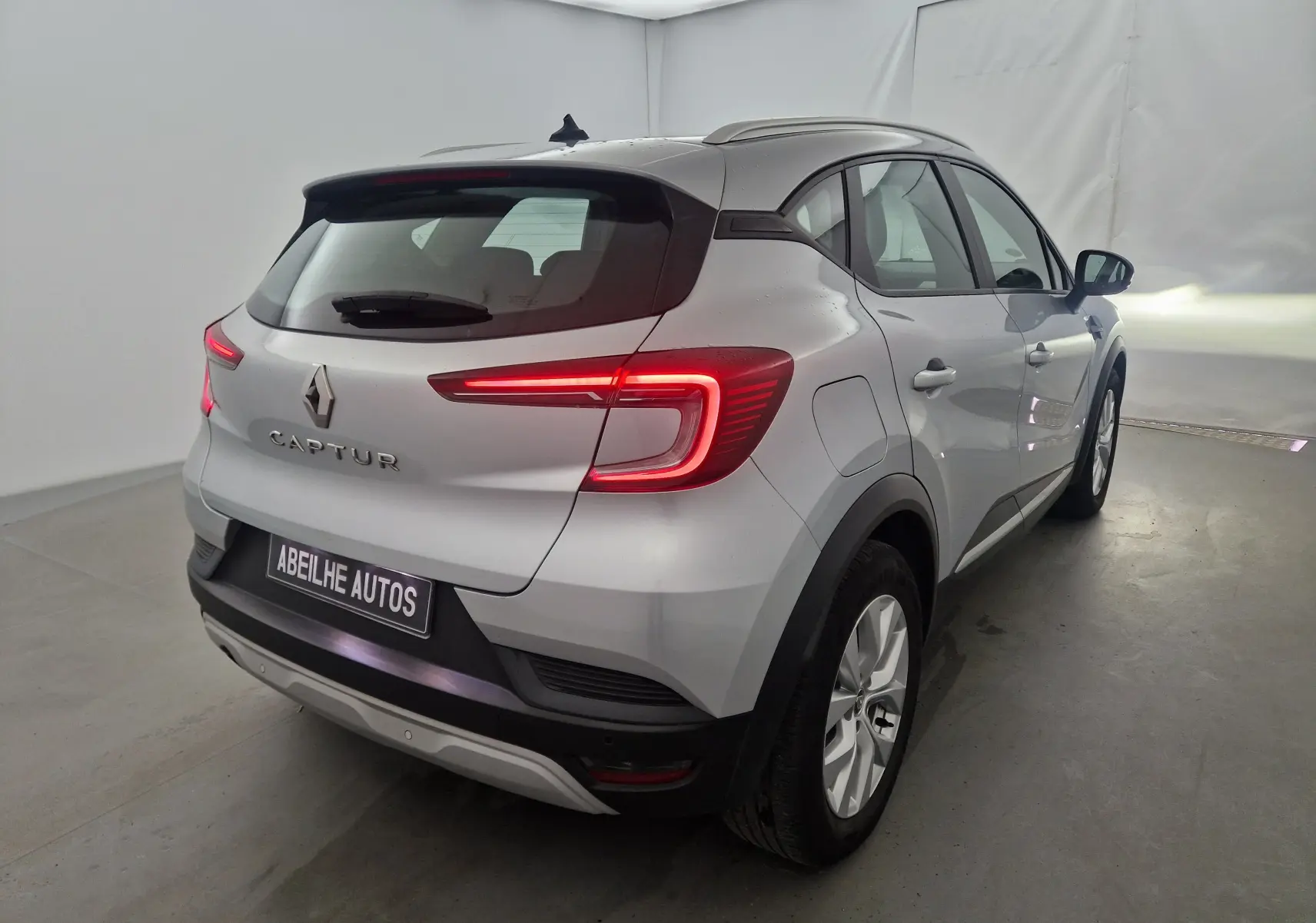 Vue 3/4 arrière droite d'un Renault Captur gris Highland avec feux arrière LED allumés dans un studio.