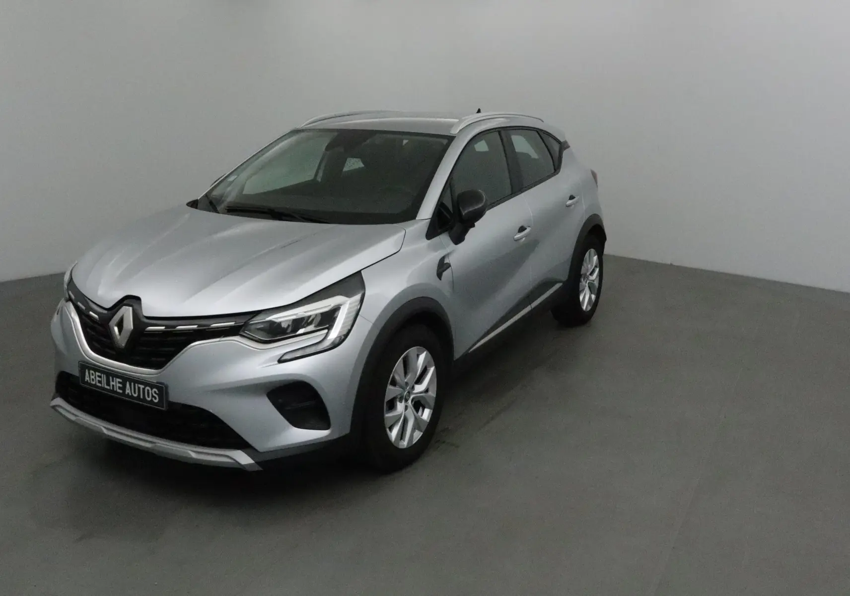 Renault Captur gris Highland en 3/4 avant droit, SUV compact avec calandre noire et jantes alliage 17 pouces.