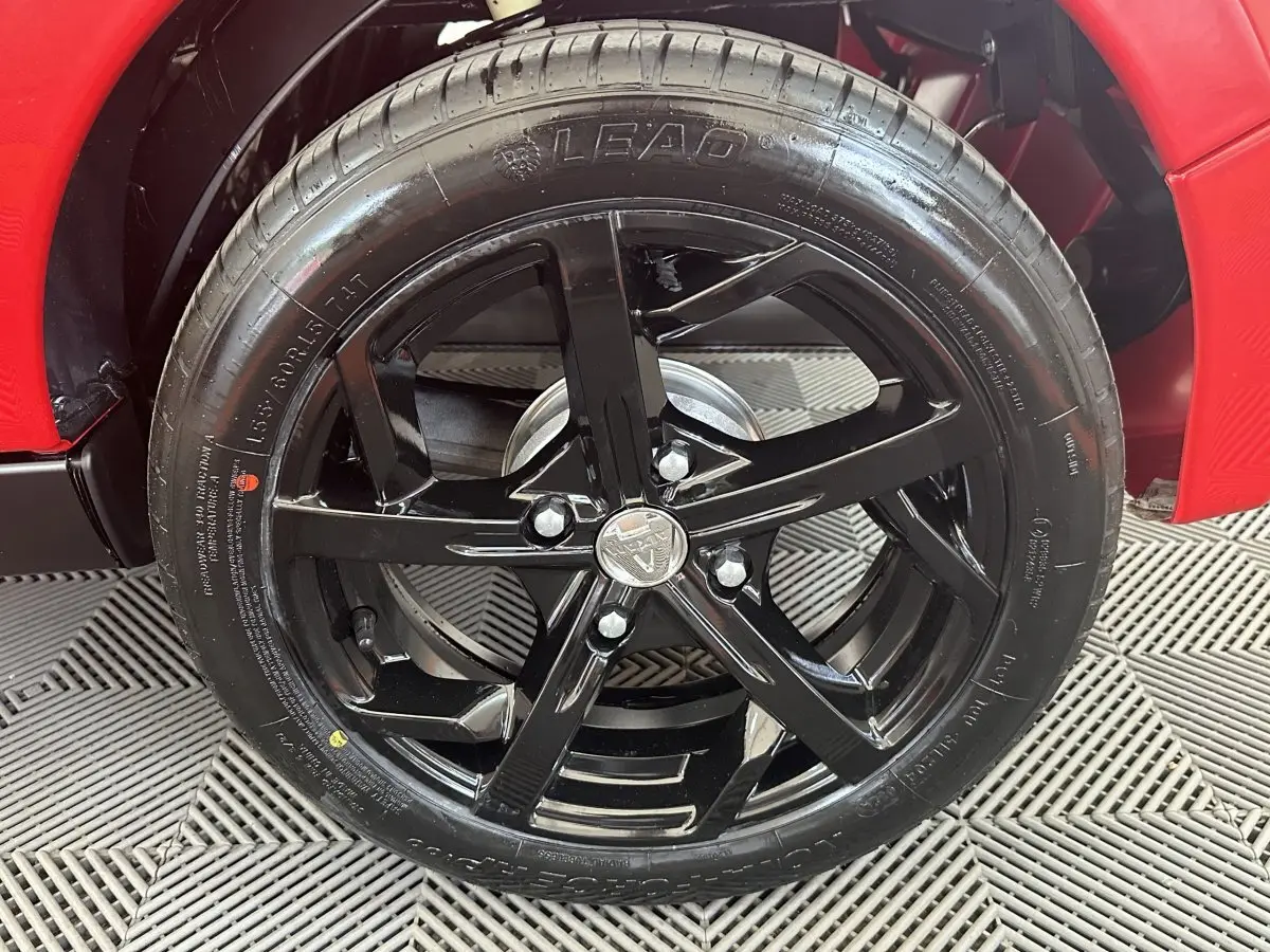 Gros plan sur la roue avant droite noire brillante d'une Aixam Ambition 0.5 City Sport rouge, avec jante cinq branches.