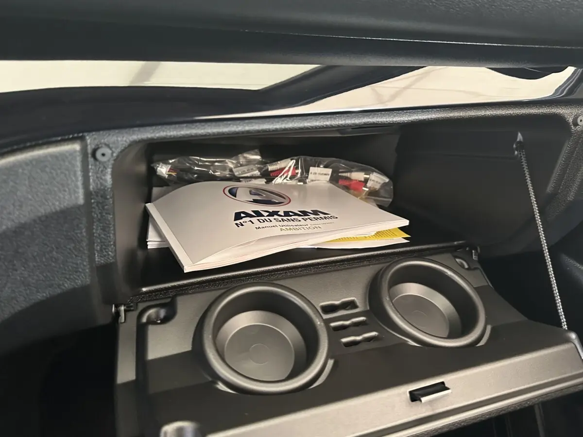 Vue intérieure du coffre à gants ouvert d'une Aixam Ambition 0.5 City Sport avec manuel et porte-gobelets visibles.