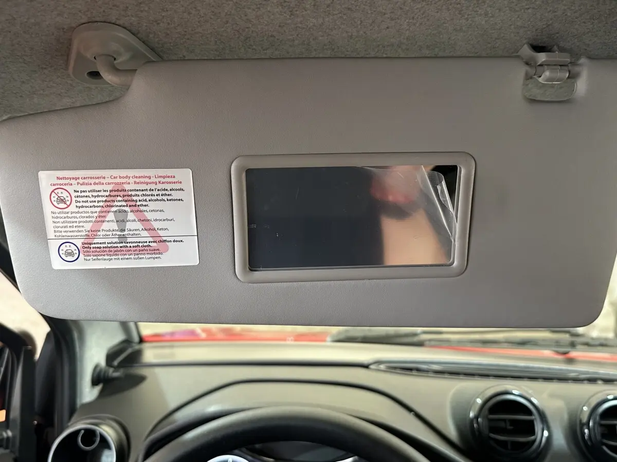 Vue intérieure centrée sur le pare-soleil avec miroir, tableau de bord et volant d'une Aixam Ambition rouge 2026.