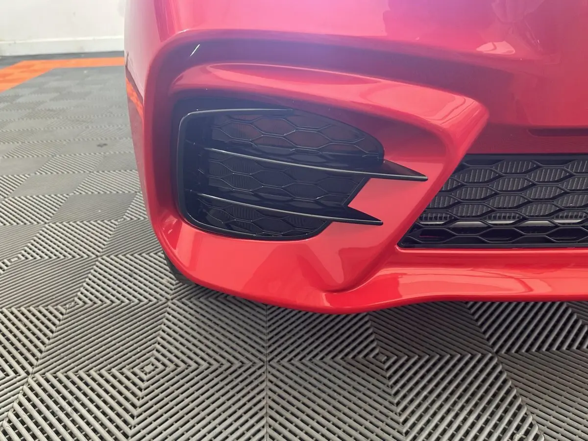 Gros plan sur la partie avant gauche rouge de l'AIXAM AMBITION 0.5 CITY SPORT 2026 avec grille noire à motif nid d'abeille.