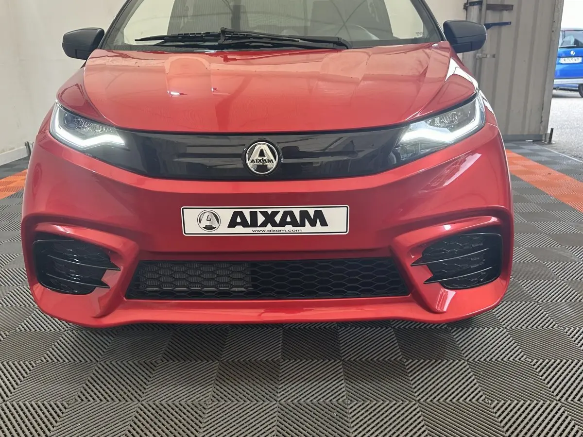 Vue frontale d'une Aixam Ambition 0.5 City Sport rouge avec phares LED et calandre noire brillante.