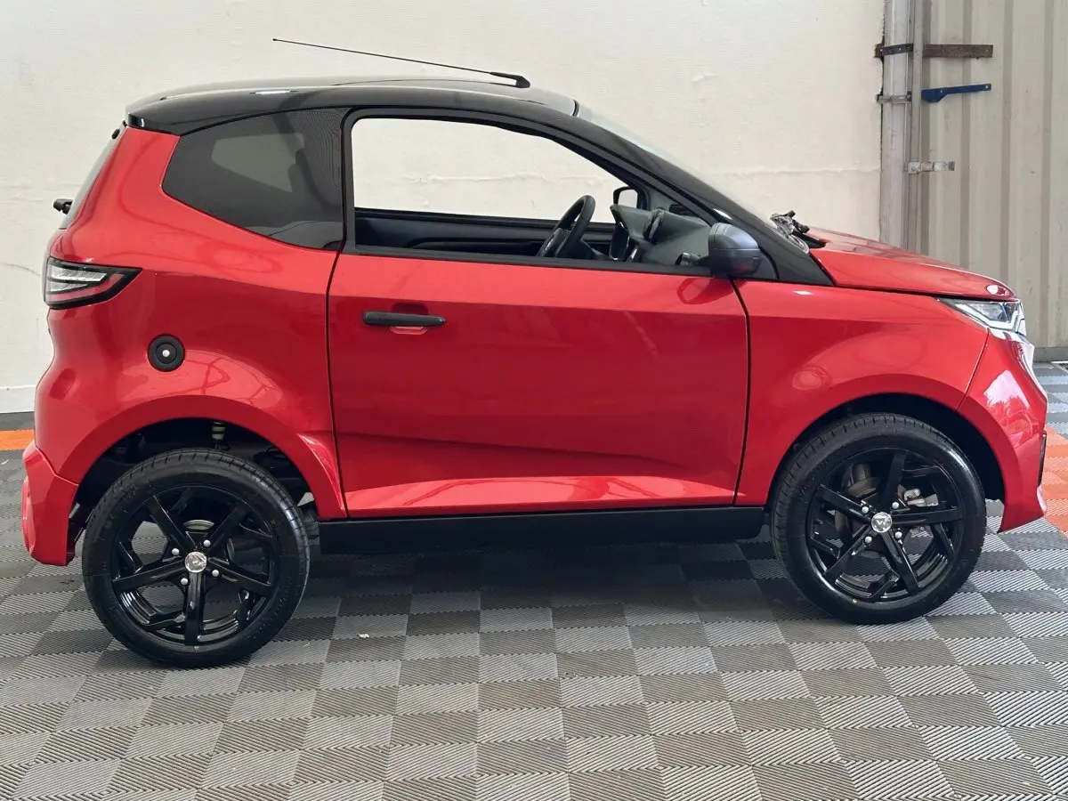 Vue de profil côté gauche d'une Aixam Ambition 0.5 City Sport rouge avec jantes noires et rétroviseur caméra.