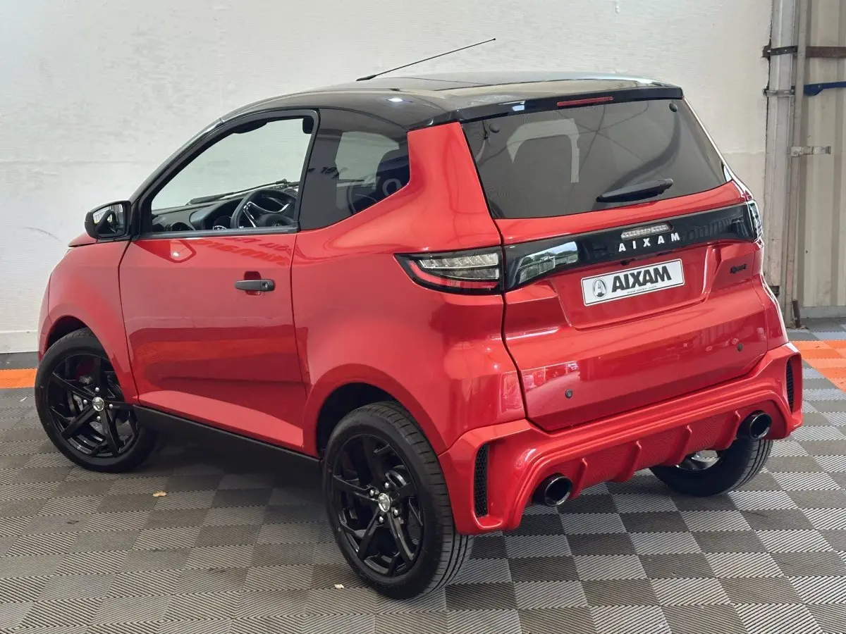 Vue 3/4 arrière droite de l'AIXAM AMBITION 0.5 CITY SPORT rouge avec toit noir et jantes noires sportives.