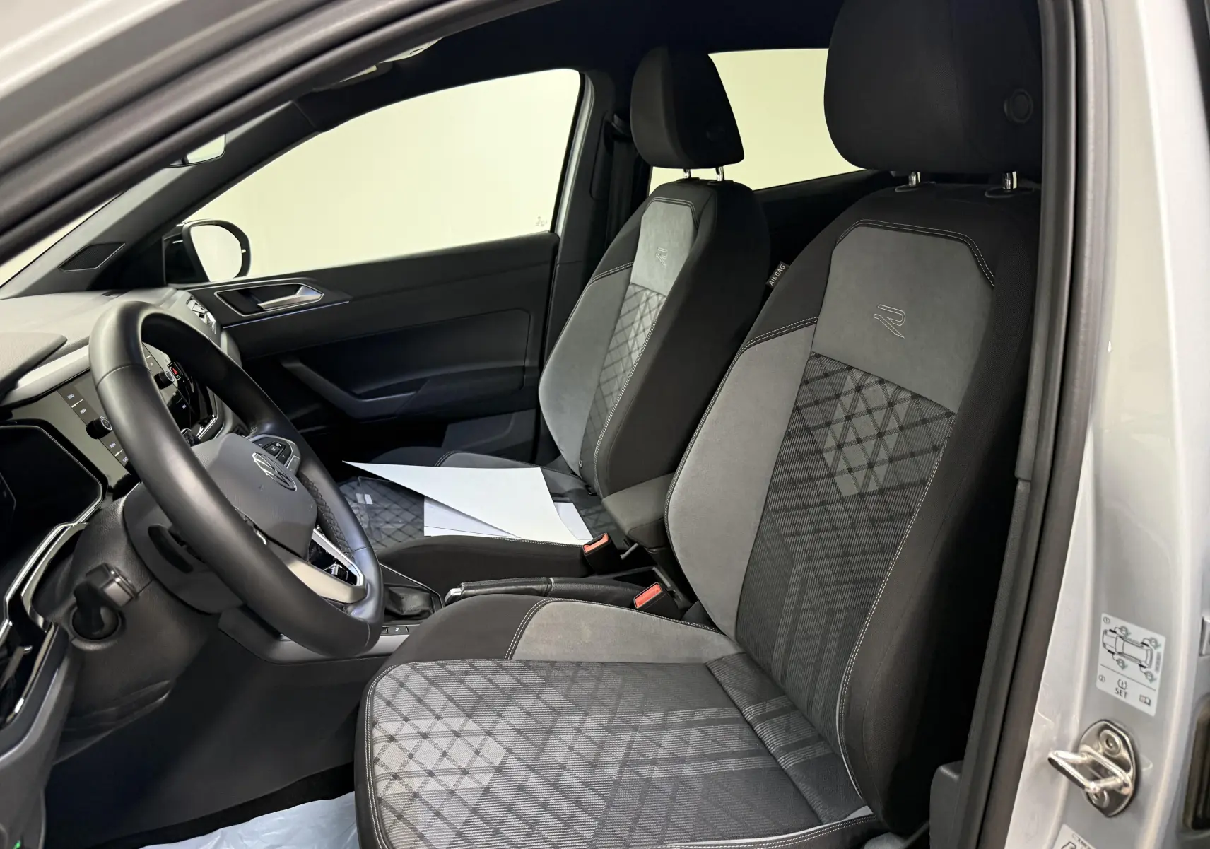 Vue intérieure côté conducteur du Volkswagen Taigo 1.5 TSI 150 DSG7 R-Line Edition avec sièges tissu gris à motifs géométriques.