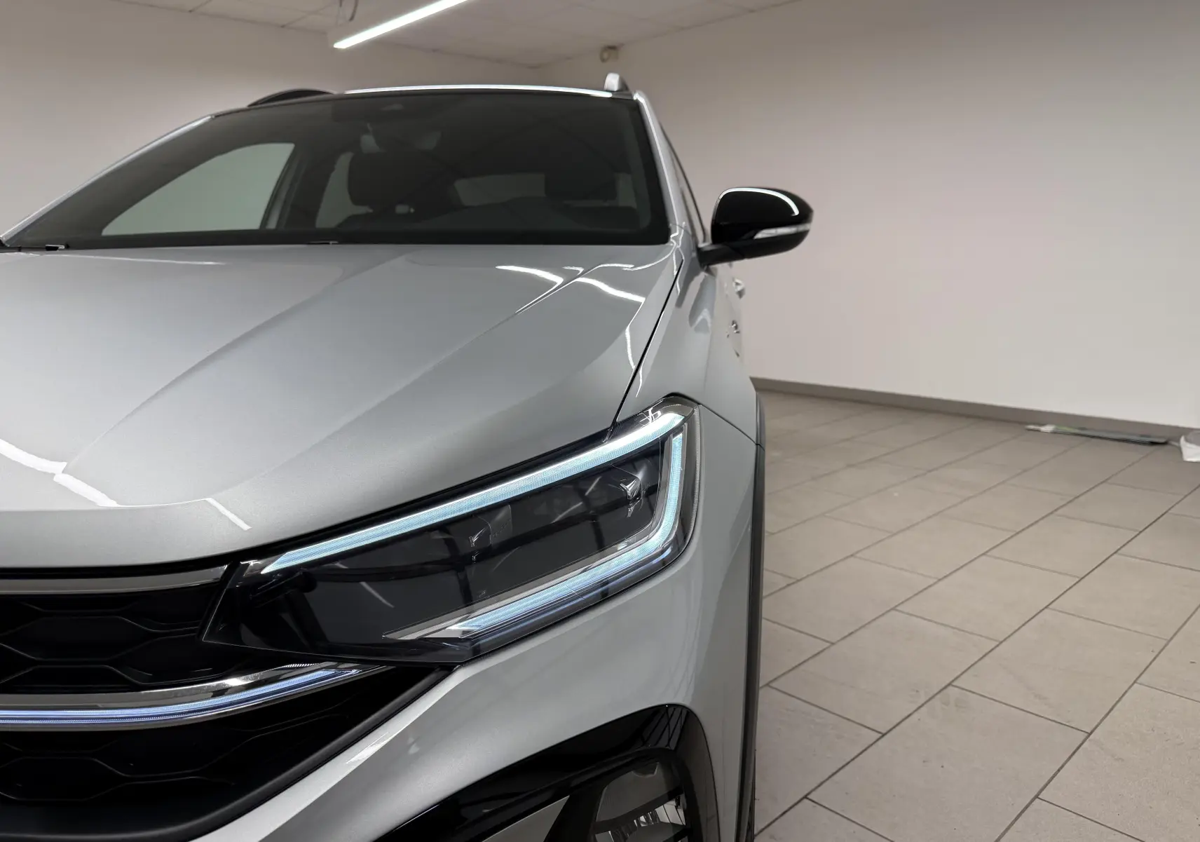 Gros plan sur l'avant droit du Volkswagen Taigo 2025 argent avec toit noir, mettant en valeur le phare LED et la calandre.