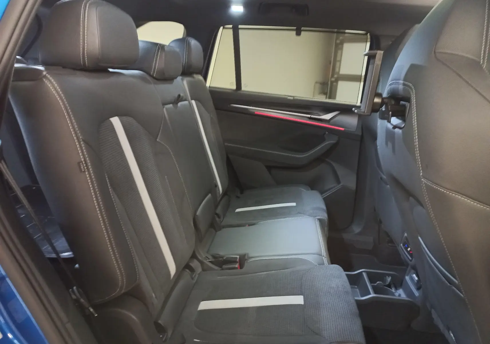 Vue intérieure côté droit des sièges arrière en cuir noir avec bandes grises et tablette intégrée sur un Skoda Kodiaq Bleu RS 2024.