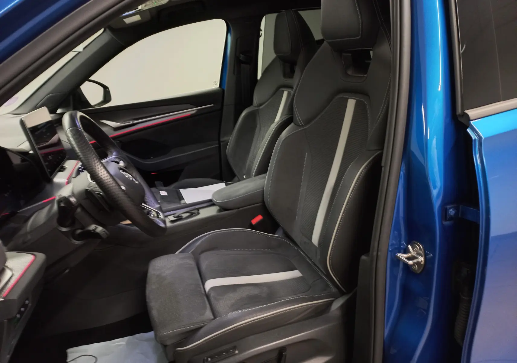 Vue intérieure côté conducteur du Skoda Kodiaq 2024 bleu RS, avec sièges sport noirs à bandes grises et tableau de bord moderne.