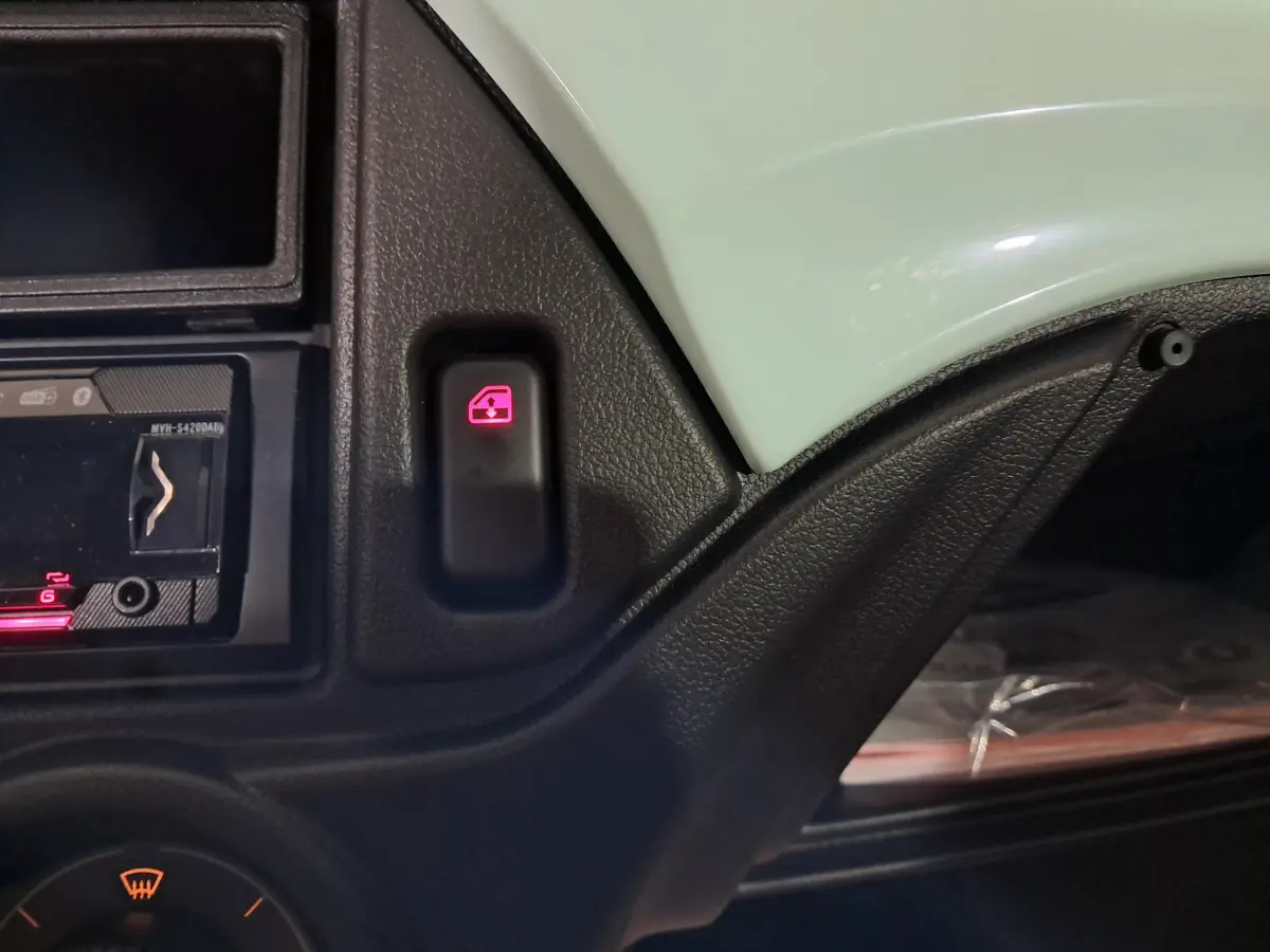 Gros plan sur le bouton de commande de lève-vitre avec tableau de bord noir et partie de la carrosserie verte côté conducteur.