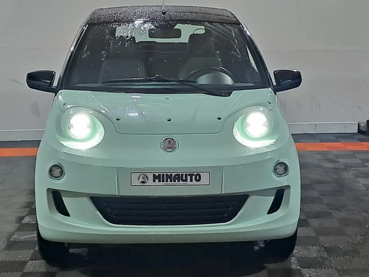 Vue frontale d'une AIXAM MINAUTO E chic 2026 verte électrique avec phares allumés et rétroviseurs caméra côté conducteur.