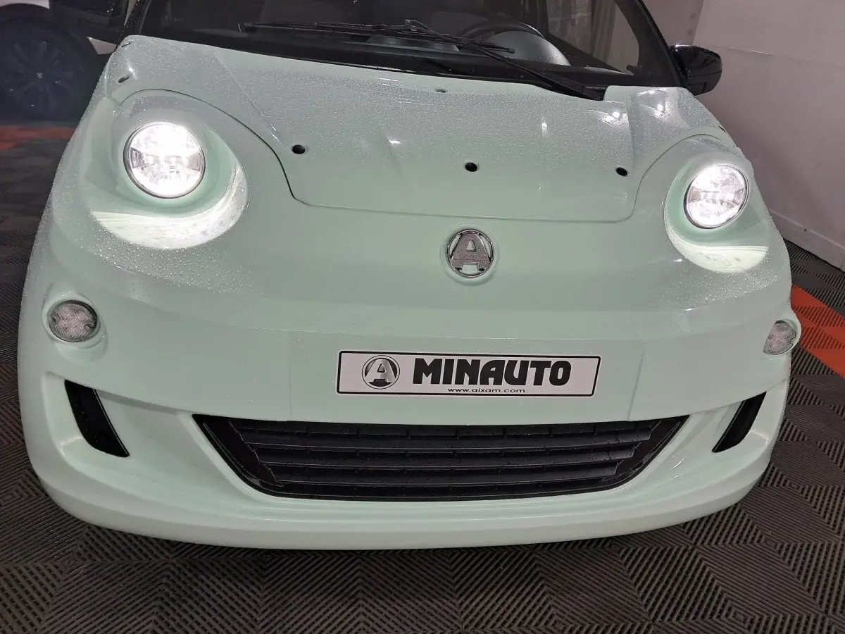 Vue avant rapprochée de l'Aixam Minauto E chic 2026 vert clair avec phares allumés et logo central visible.