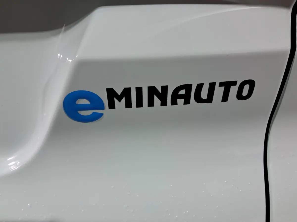 Détail du logo eMINAUTO en bleu et noir sur la carrosserie blanche d'un véhicule Aixam MINAUTO E chic 2026.