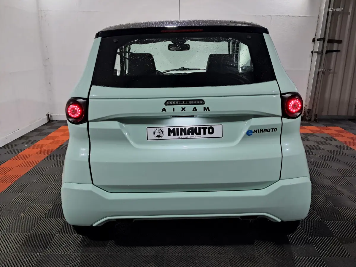 Vue arrière d'une AIXAM MINAUTO E chic 2026 vert clair avec feux ronds allumés et logo eMINAUTO visible à droite.