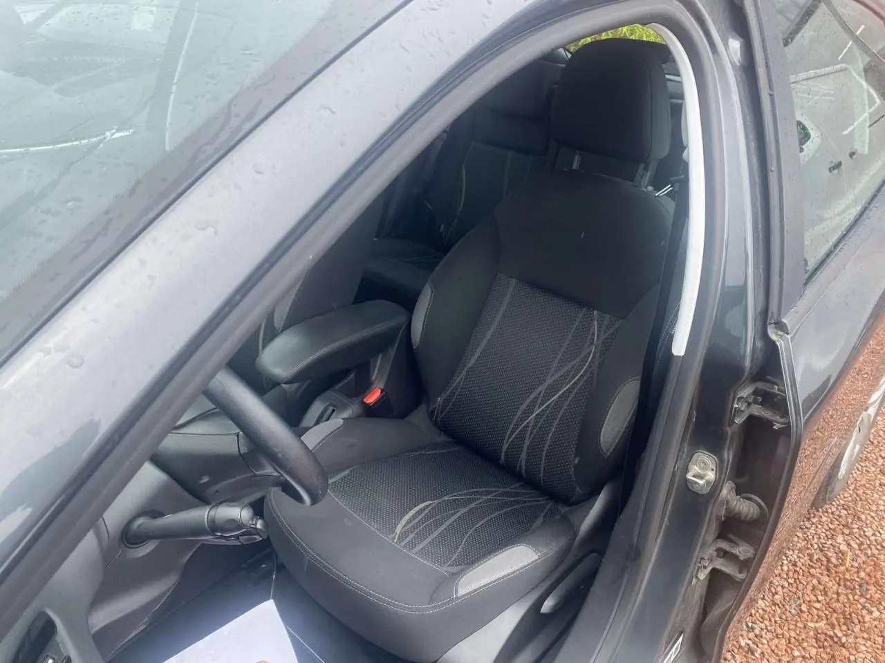 Intérieur côté conducteur d'une Peugeot 208 gris shark 2013, siège tissu avec accoudoir central visible.