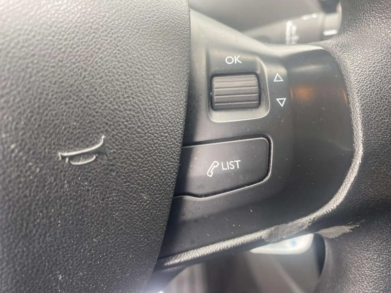 Gros plan sur les commandes multifonctions du volant noir de la Peugeot 208 gris Shark de 2013.