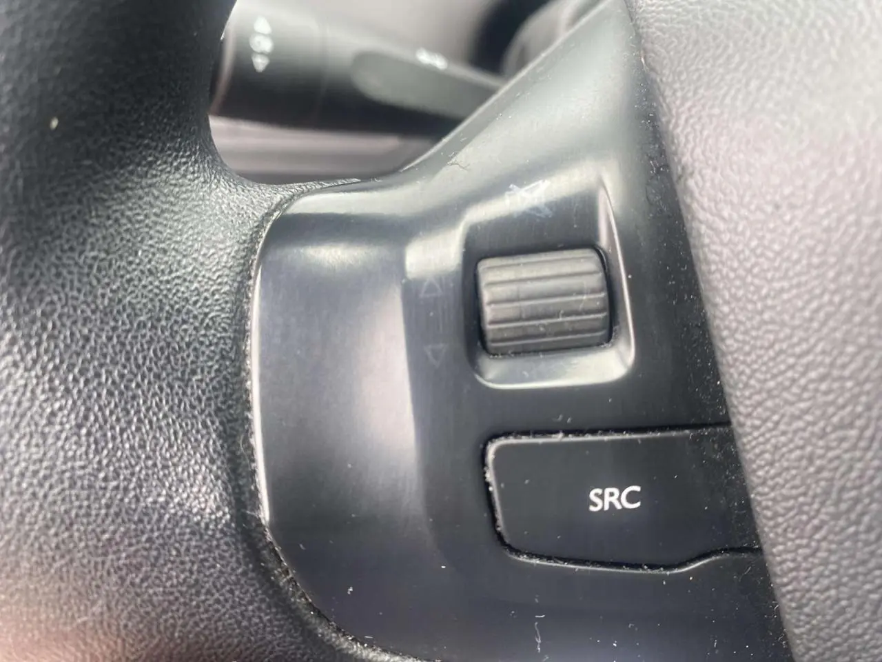 Gros plan sur les commandes multifonctions du volant noir d'une Peugeot 208 gris Shark de 2013.