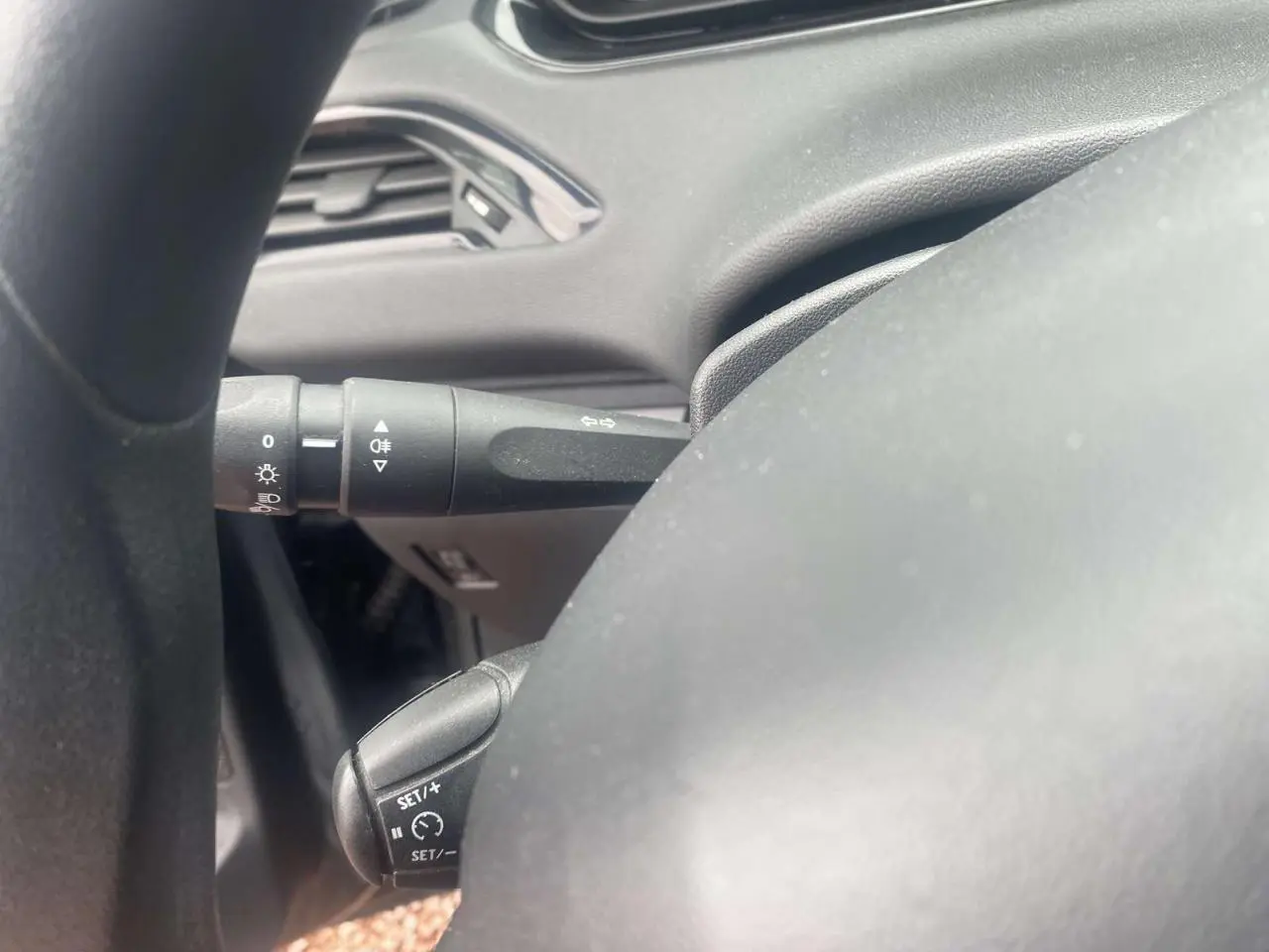 Gros plan sur le volant multifonction noir de la Peugeot 208 gris Shark, avec commandes de régulateur et clignotants.